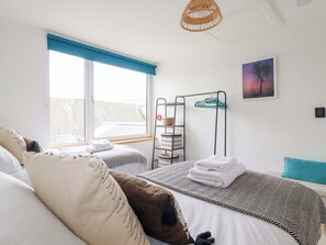 Ein Schlafzimmer mit zwei Betten, einem Fenster mit blauen Jalousien, einem Wandregal mit Körben, einer Pendelleuchte und einem gerahmten Bild.