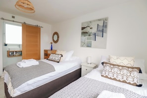 A hotel room with two beds, a wooden door, a mirror, a wall art piece, and a nightstand with a lamp. - La Casita (Newquay)