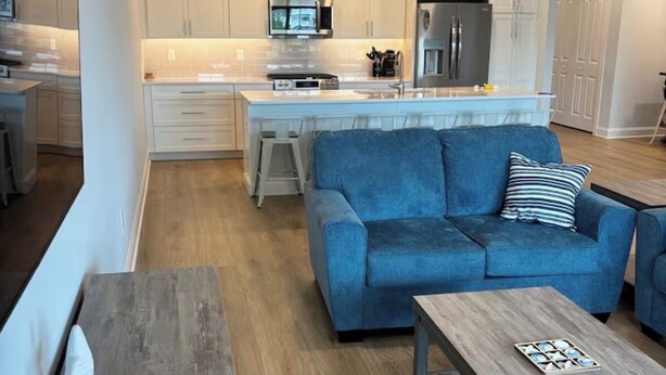 Una cocina moderna con armarios blancos, una isla central y un sofá azul en la sala de estar.