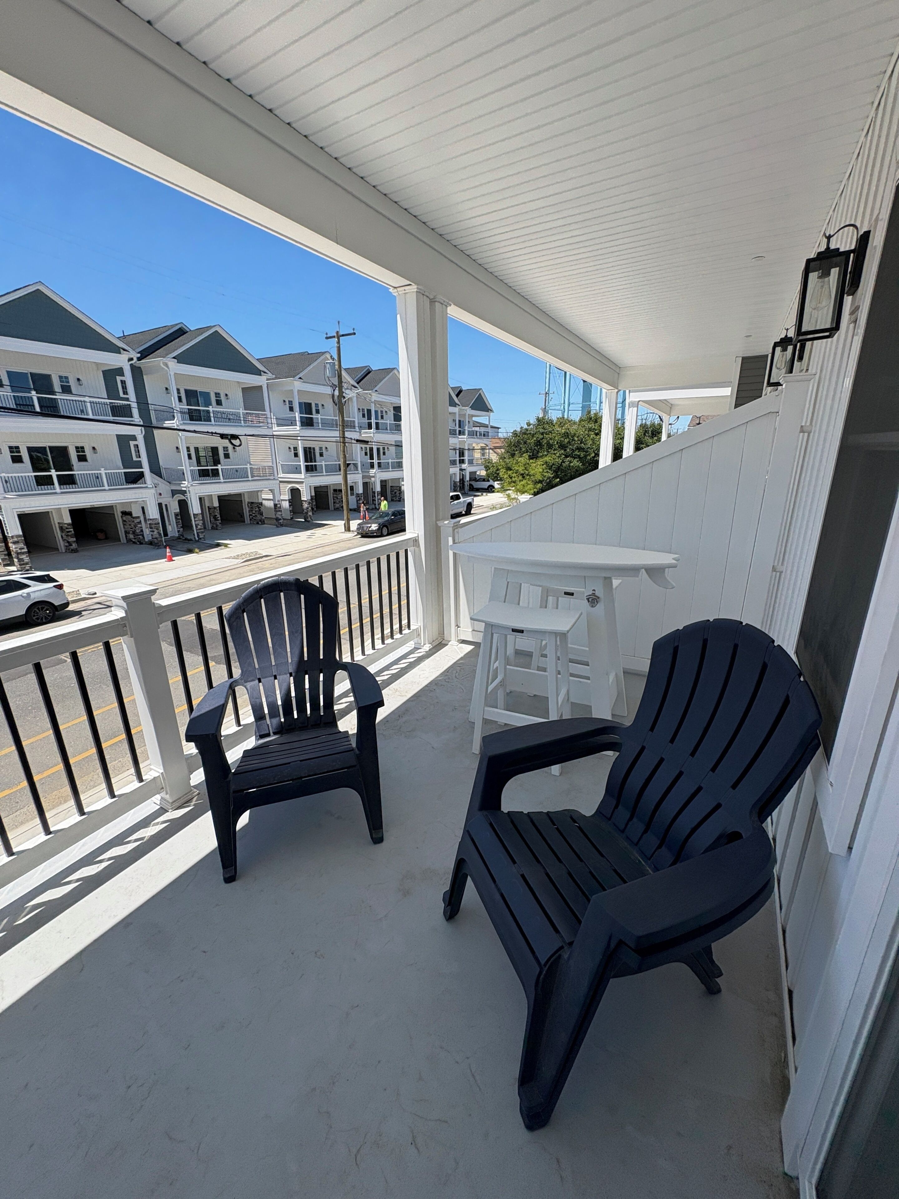 A covered balcony with two Adirondack chairs and a small white table.