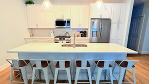 Una cocina moderna con armarios blancos, electrodomésticos de acero inoxidable, una isla grande con taburetes y luces colgantes.