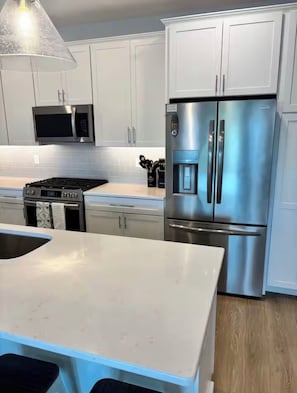A modern kitchen with white cabinets, a stainless steel refrigerator, a microwave, and a gas stove.