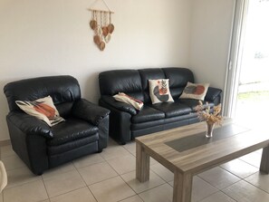Ein Wohnzimmer mit zwei schwarzen Ledersofas, einem Holztisch und einer Wanddekoration aus Makramee.
