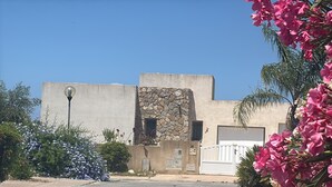 Un bâtiment à la façade en pierre, doté d’un portail blanc et entouré de verdure.