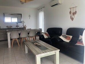 Ein modernes Wohnzimmer mit Essbereich, einem schwarzen Ledersofa und einem Holztisch.