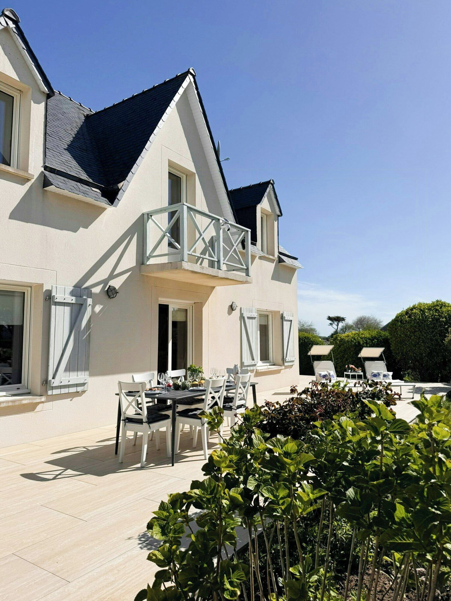 A two-story house with a balcony, outdoor seating, and a garden.