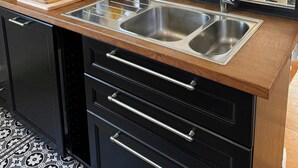 Une cuisine moderne dotée d’un grand miroir, de deux éviers en acier inoxydable, d’un plan de travail en bois et offrant une vue sur l’espace repas grâce au miroir.