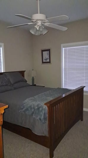 Ein Schlafzimmer mit einem Bett, einem Deckenventilator, einem Fenster mit Jalousien und einem gerahmten Bild an der Wand.