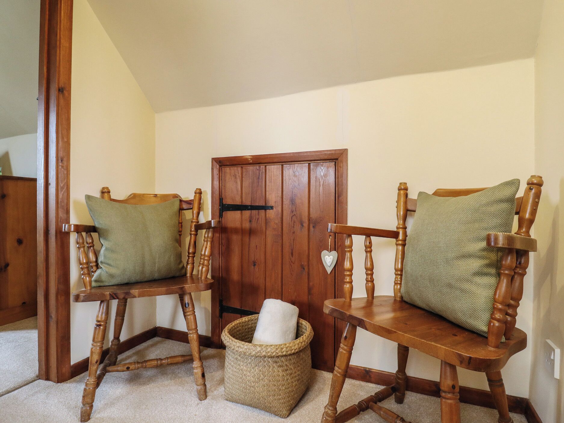 A room with two wooden chairs with cushions, a wooden door, and a woven basket on the floor.