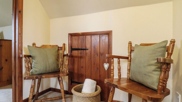 Una habitación con dos sillas de madera con cojines, una puerta de madera y una cesta tejida en el suelo.