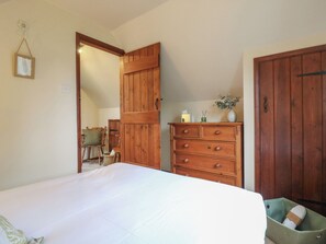 A bedroom with a bed, wooden dresser, and a green storage bin. - Barclay Cottage (Ashford)