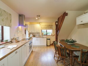 A kitchen with white cabinets, a wooden countertop, and a dining area with a table and chairs. - Barclay Cottage (Ashford)