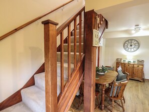 A wooden staircase leading to a dining area with a table and chairs, a clock on the wall, and a cabinet with baskets. - Barclay Cottage (Ashford)