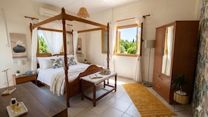 A bedroom with a four-poster bed, a bedside table with a lamp, a bedside plant, and a window with curtains. - Villa Christina 2BR Pool Retreat (Paralimni)