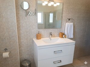A bathroom with a white vanity, a round mirror, a large rectangular mirror, a towel rack, and a trash bin. - Villa Christina 2BR Pool Retreat (Paralimni)