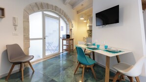 Un comedor con una mesa preparada para dos, un televisor montado en la pared y un arco de piedra que da a un balcón.