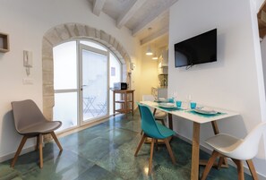 Ein Essbereich mit einem Tisch für zwei Personen, einem an der Wand montierten Fernseher und einem steinernen Bogen, der auf einen Balkon führt.