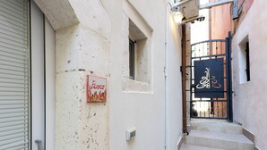 Un callejón estrecho con una puerta de tienda cerrada, una ventana pequeña y una reja con un cartel decorativo.