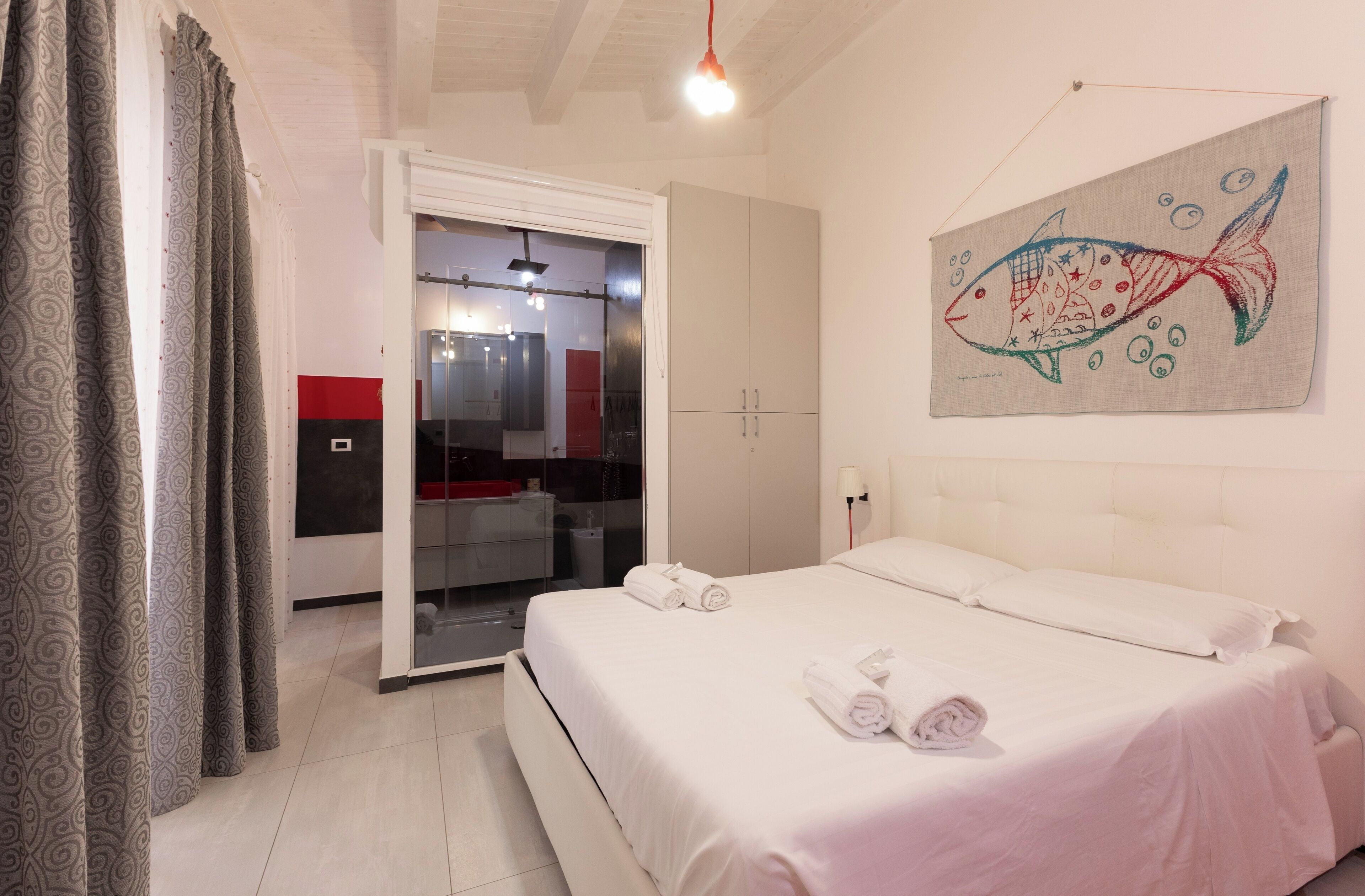 A bedroom with a bed, a towel, a fish painting, and a door leading to a bathroom.