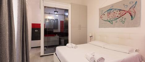 A bedroom with a bed, a towel, a fish painting, and a door leading to a bathroom.