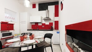 A modern kitchen with a dining area, white cabinets, red accents, a glass table, and a built-in fish tank. - LE CORTI - Fuoco by OrtigiaApartments (Syracuse)