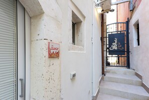 Ein schmaler Gang mit einer geschlossenen Schaufenstertür, einem kleinen Fenster und einem Tor mit einem verzierten Schild.