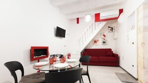 A modern living space with a dining area, a red sofa, and a staircase leading to an upper level. - LE CORTI - Fuoco by OrtigiaApartments (Syracuse)