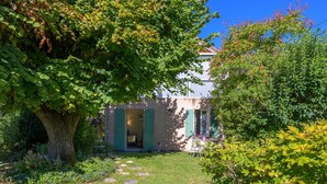 Un giardino che conduce a un edificio con persiane verdi, un vialetto in pietra e un grande albero.