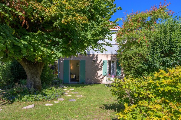 A garden with a pathway leading to a building with green shutters.