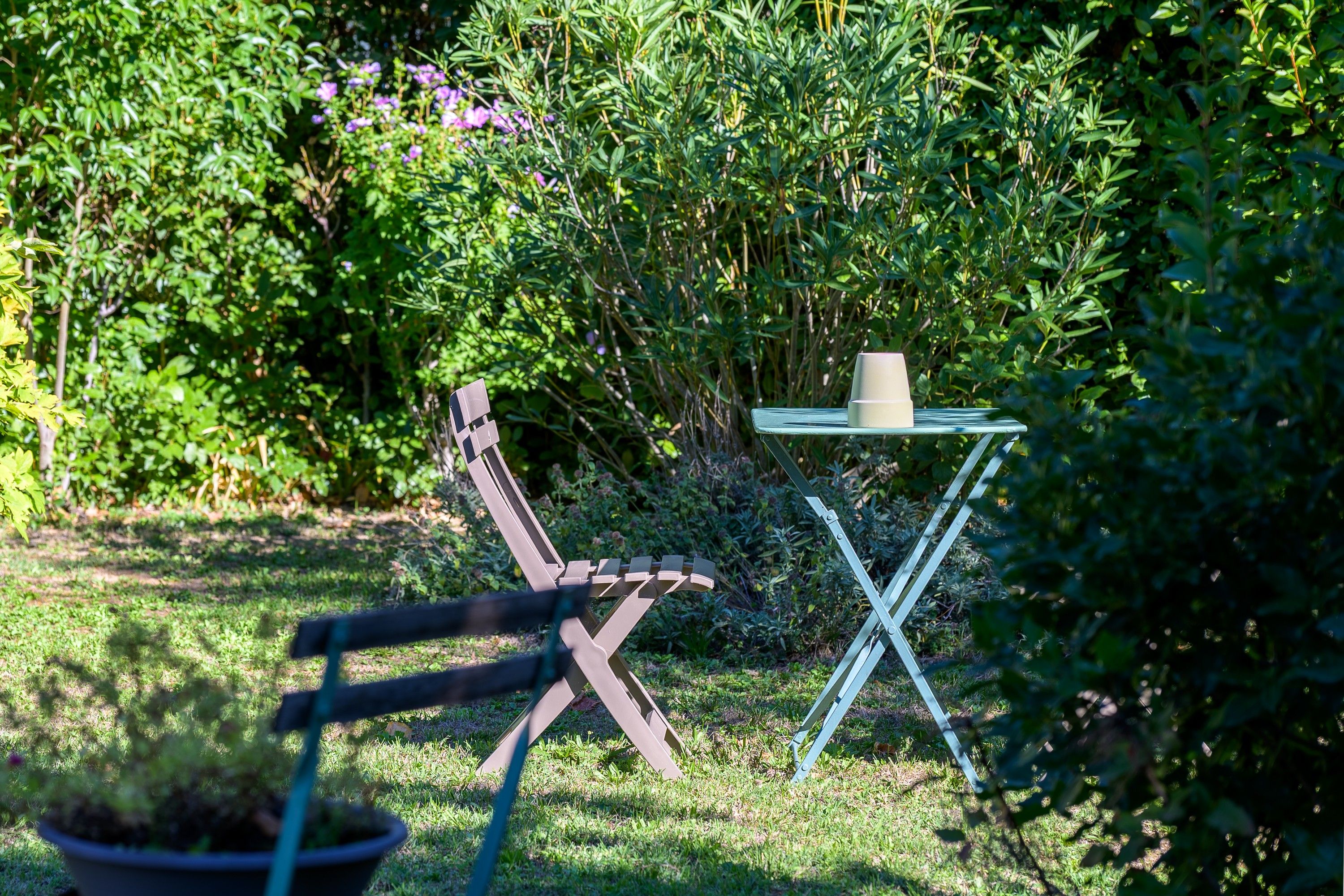 Een tuin met een metalen tafel en een stoel, omringd door groen en bloemen.