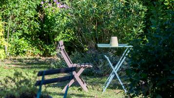 Een tuin met een metalen tafel en een stoel, omringd door groen en bloemen.