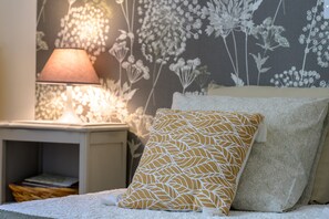 A neatly made bed with a patterned pillow, a bedside lamp, and a floral wallpaper. - Gîte Des Pivoines: Romantic Getaway in the South (Buis-les-Baronnies)