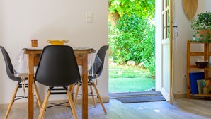 Zona pranzo con tavolo, sedie e vista su un giardino tramite una porta aperta.