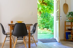 A dining area with a table, chairs, and a view of a garden through an open door. - Gîte Des Pivoines: Romantic Getaway in the South (Buis-les-Baronnies)