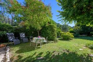 An outdoor seating area with a table and chairs, surrounded by lush greenery and trees.