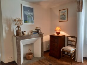 Une pièce avec une cheminée, une chaise en bois, une lampe, une bibliothèque et un tableau accroché au mur.