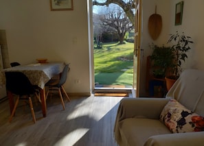 Une pièce comprenant une table à manger, un canapé et donnant sur un jardin grâce à une porte ouverte.