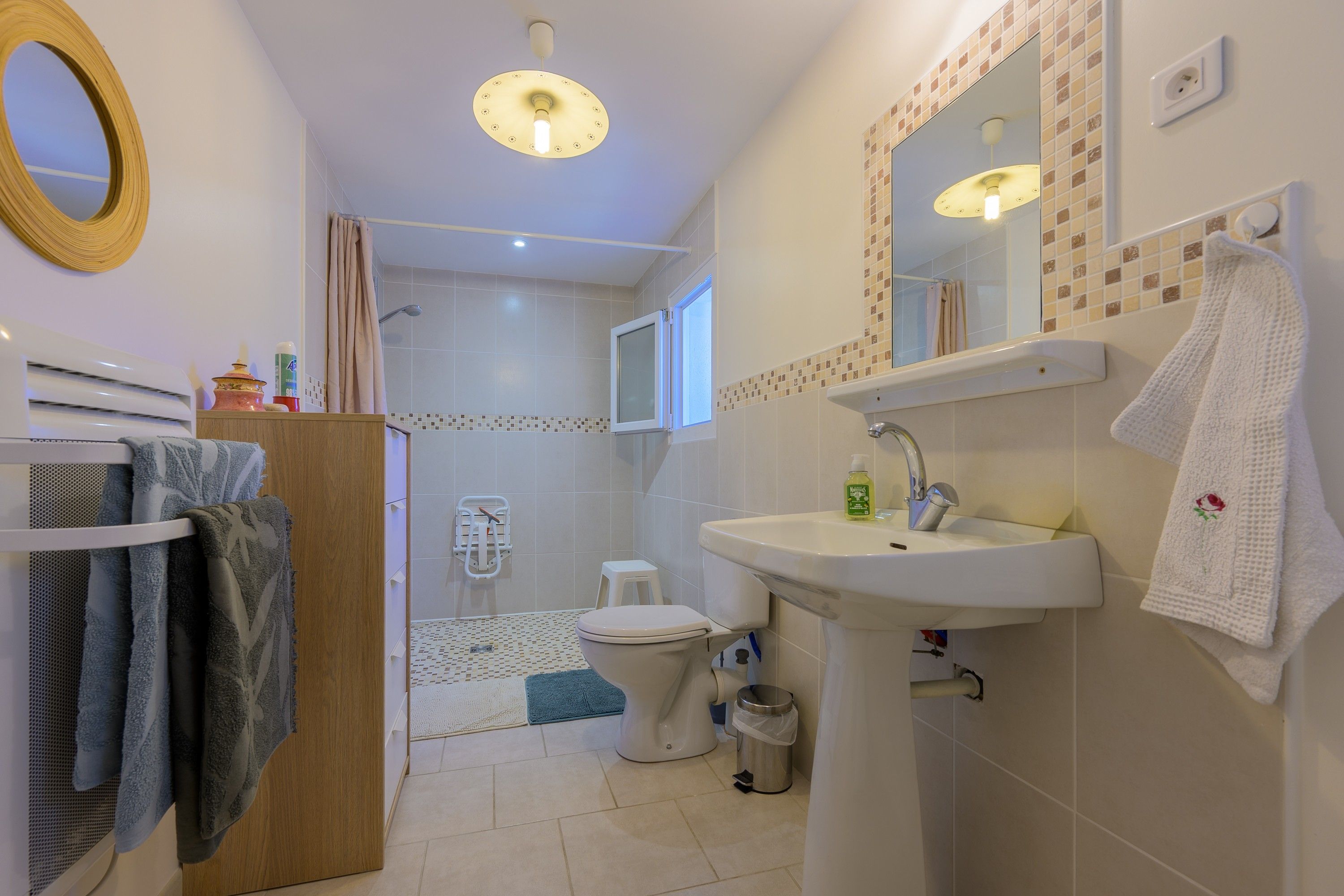 Une salle de bain équipée d’un WC, d’un lavabo et d’une douche. On y trouve un porte-serviettes avec des serviettes, un miroir et un luminaire au plafond.