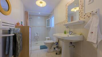 Une salle de bain équipée d’un WC, d’un lavabo et d’une douche. On y trouve un porte-serviettes avec des serviettes, un miroir et un luminaire au plafond.