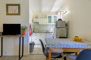 A compact kitchen with white cabinets, a Bosch dishwasher, a microwave, and a refrigerator. There's a dining table with chairs and a TV on a stand. - Gîte Des Pivoines: Romantic Getaway in the South (Buis-les-Baronnies)
