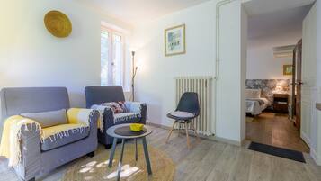 Un salon avec un canapé gris, un fauteuil plus petit, une petite table sur laquelle se trouve un bol jaune, et un radiateur.