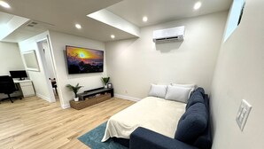 Un dormitorio moderno con una cama, un televisor, un escritorio y una planta pequeña.