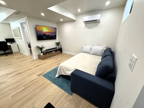 Ein modernes Schlafzimmer mit Bett, Fernseher, Schreibtisch und einer kleinen Pflanze.
