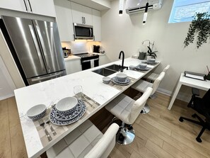 Eine moderne Küche mit einem Edelstahl-Kühlschrank, einer Mikrowelle und einem langen Esstisch, gedeckt mit weißen und blauen Tellern, Besteck und Gläsern.