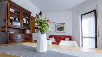 A room with a wooden table, a white vase with flowers, a red sofa, and a cabinet with glass doors.
