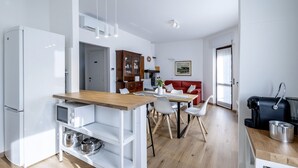 Une cuisine moderne avec un plan de travail en bois, des meubles blancs et un coin repas agrémenté d’un canapé rouge.