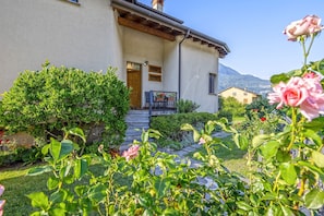 Una casa con un giardino, una porta di legno e una montagna sullo sfondo.