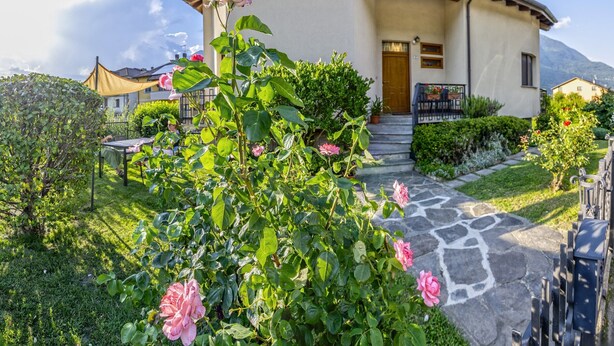 Une maison avec un toit incurvé, un chemin de pierre menant à l’entrée et une végétation luxuriante.