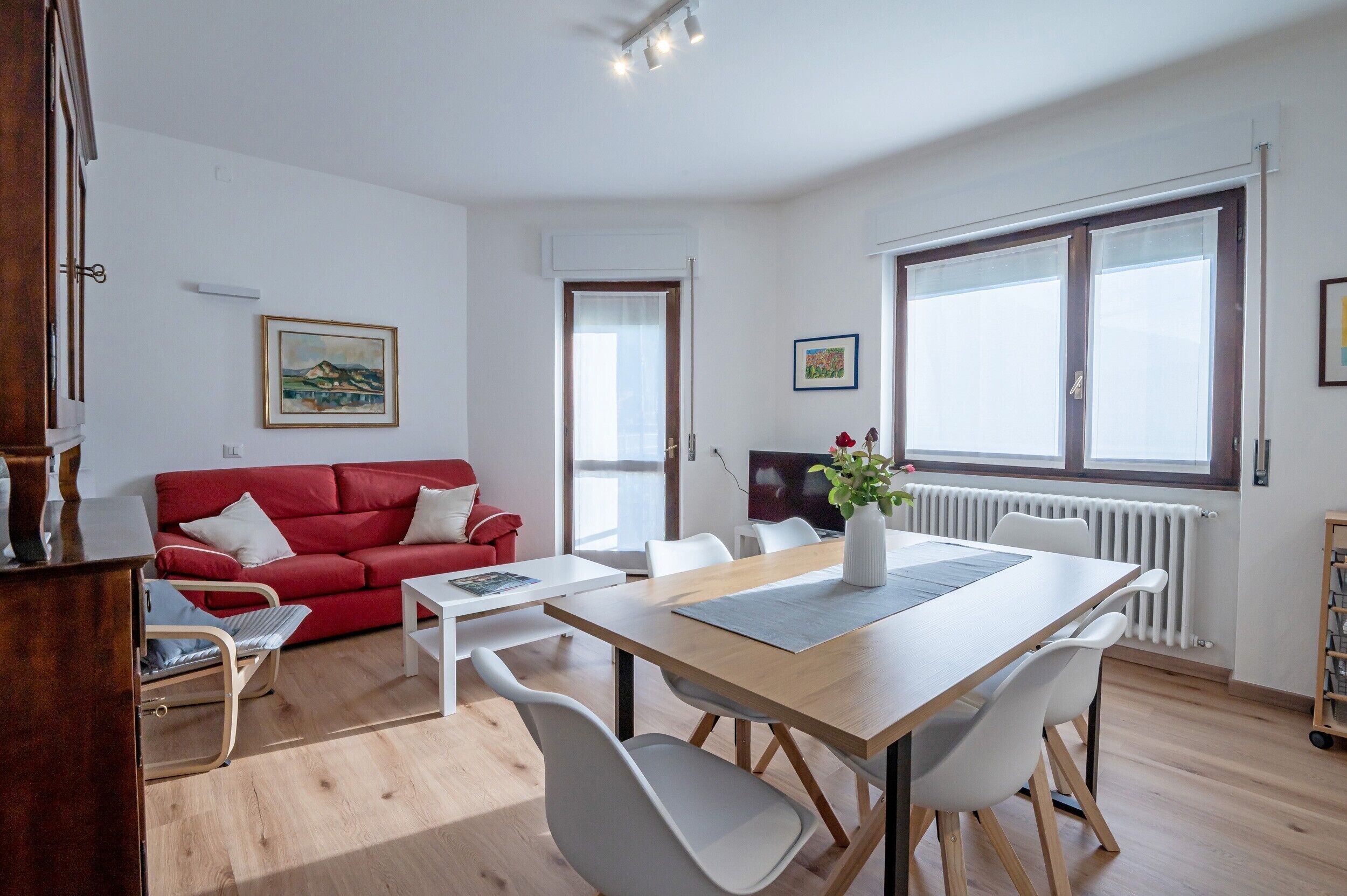 Ein modernes Wohnzimmer mit einem roten Sofa, weißen Sesseln, einem Holzespeisetisch und einem Fernseher.