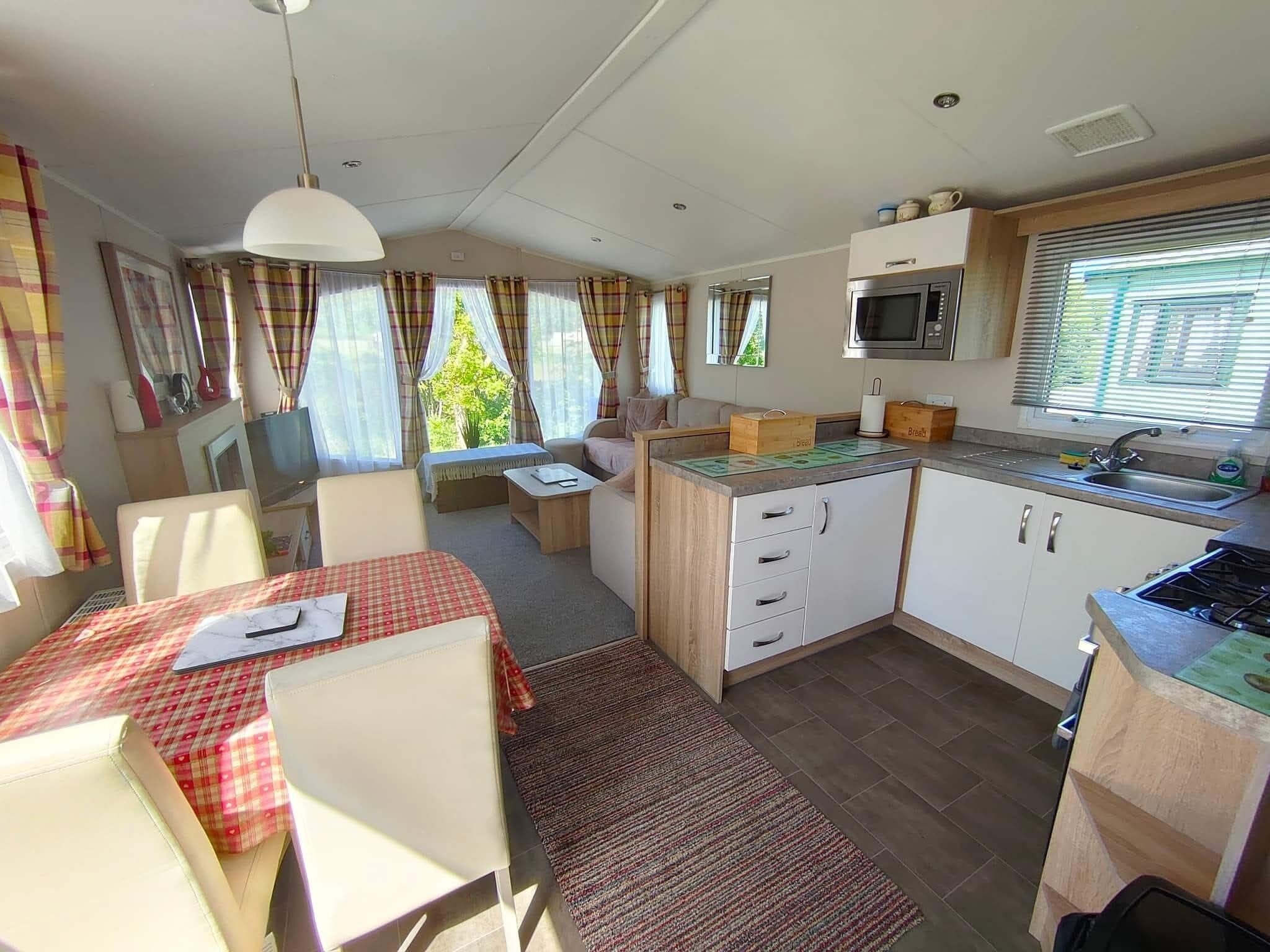 A compact kitchen with a microwave, sink, and wooden cabinets. There is a dining area with a table and chairs, and a small seating area with a sofa.